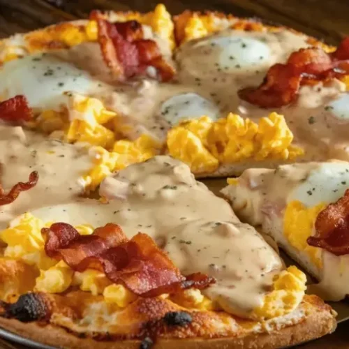 A breakfast pizza topped with scrambled eggs, crispy bacon, sausage gravy, and melted cheese, cut into slices.