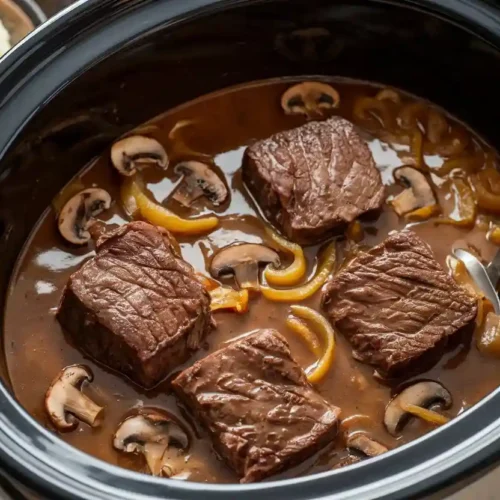 Slow-cooked Venison Cube Steaks in a rich mushroom and onion gravy inside a Crockpot.