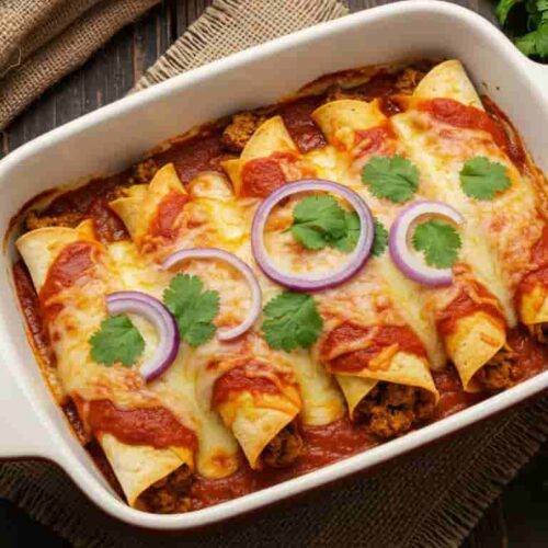 Homemade Boulders enchilada recipe featuring rolled corn tortillas filled with meat, topped with red enchilada sauce, melted cheese, red onions, and fresh cilantro in a white ceramic baking dish