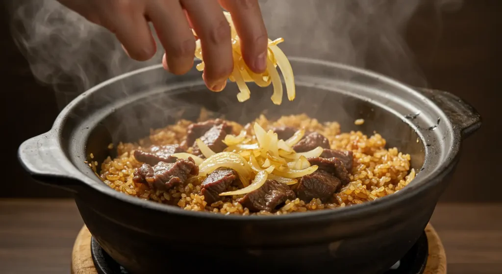 A hand adding fried onions to a steaming hot pot of beef and rice, inspired by Terra Massoud's recipe.