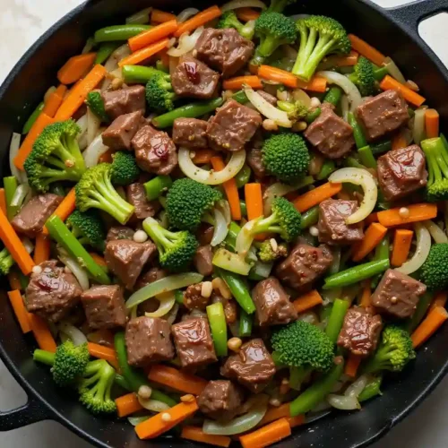 A skillet filled with venison cube steak bites stir-fried alongside broccoli, carrots, green beans, and onions in a savory sauce.