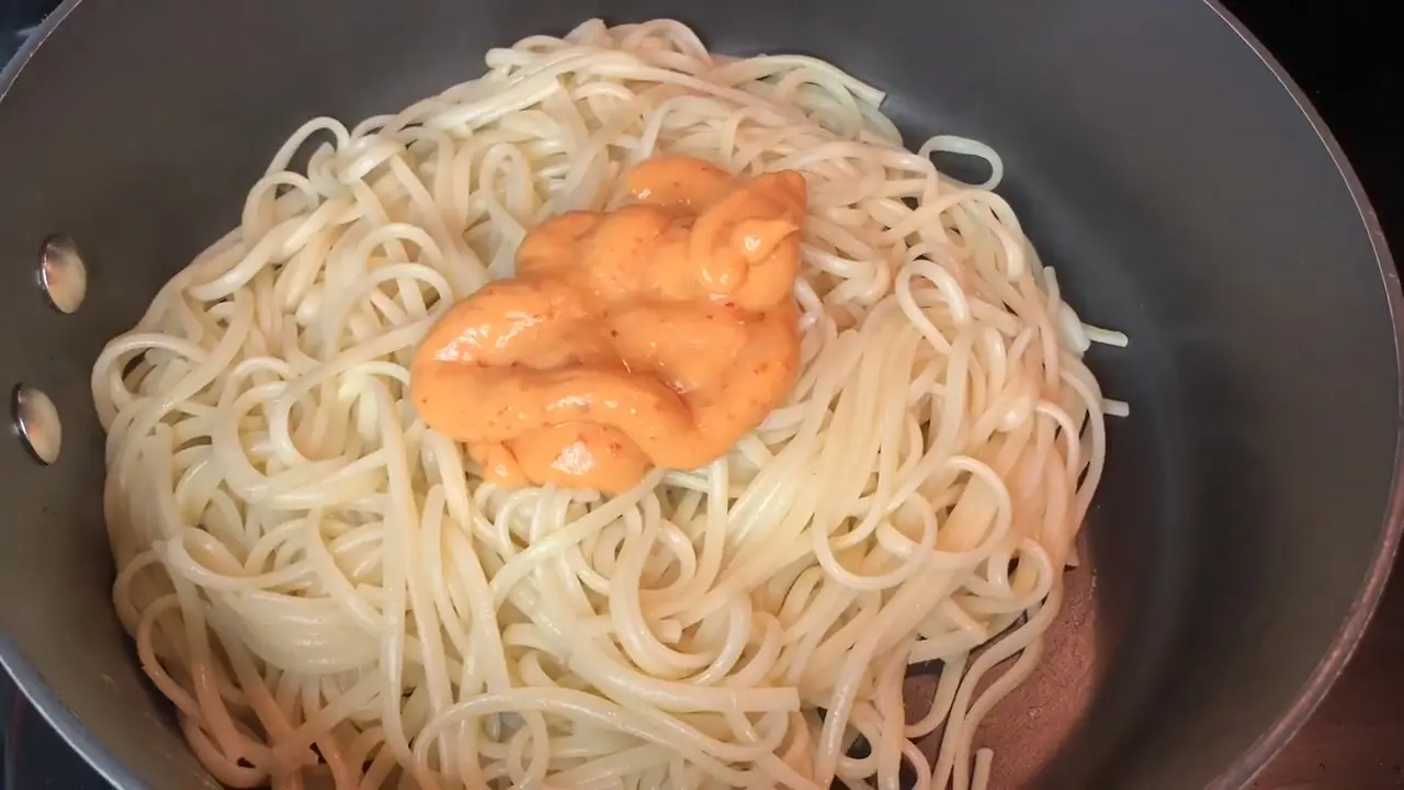 Cooked noodles in a pan with orange Boom Boom sauce being added to the center