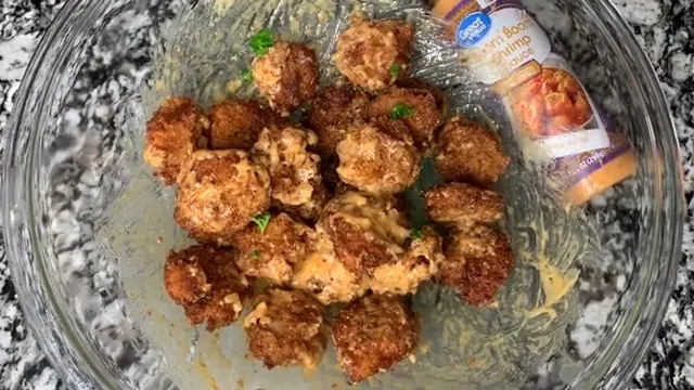 Crispy Boom Boom Shrimp in a glass bowl with sauce and green herbs on a granite countertop