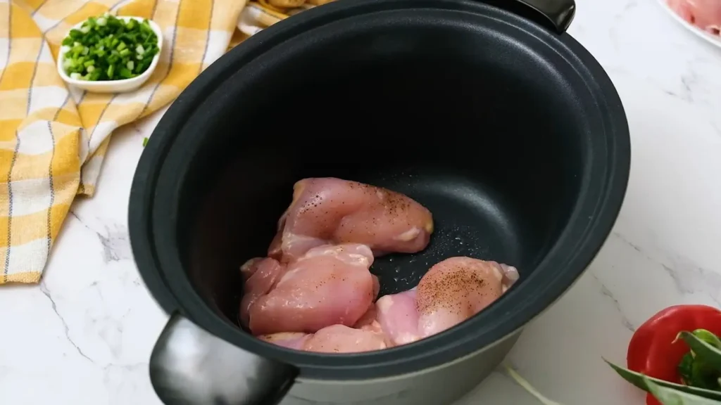  Raw chicken pieces seasoned with spices in a black crockpot for sweet Hawaiian crockpot chicken