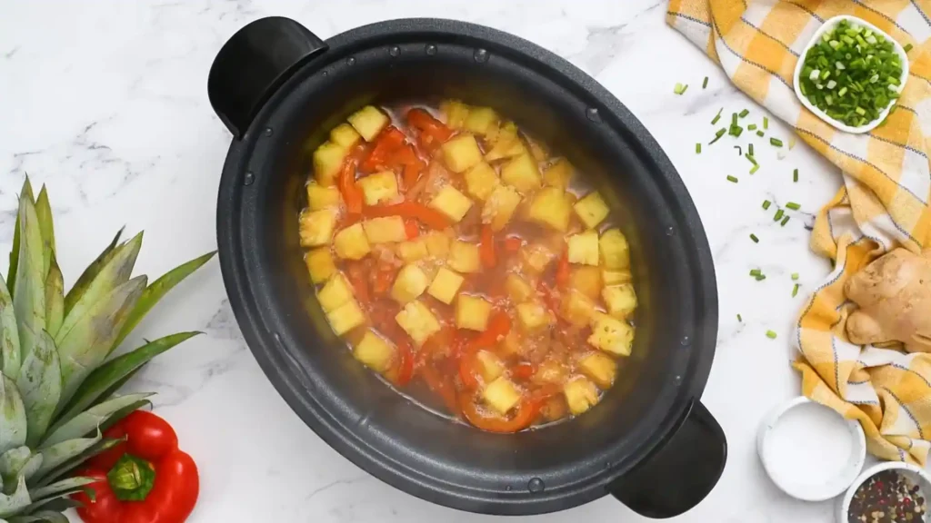 Sweet Hawaiian crockpot chicken with pineapple chunks and red bell peppers cooking in a slow cooker