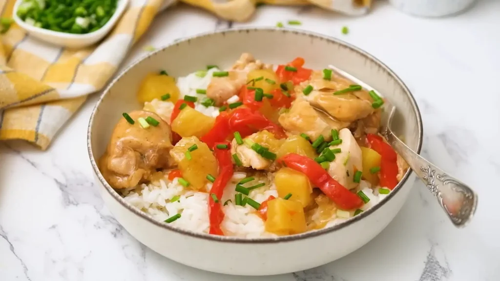 A bowl of Sweet Hawaiian Crockpot Chicken served over white rice, featuring tender chicken, red bell peppers, and pineapple chunks, garnished with fresh green onions.