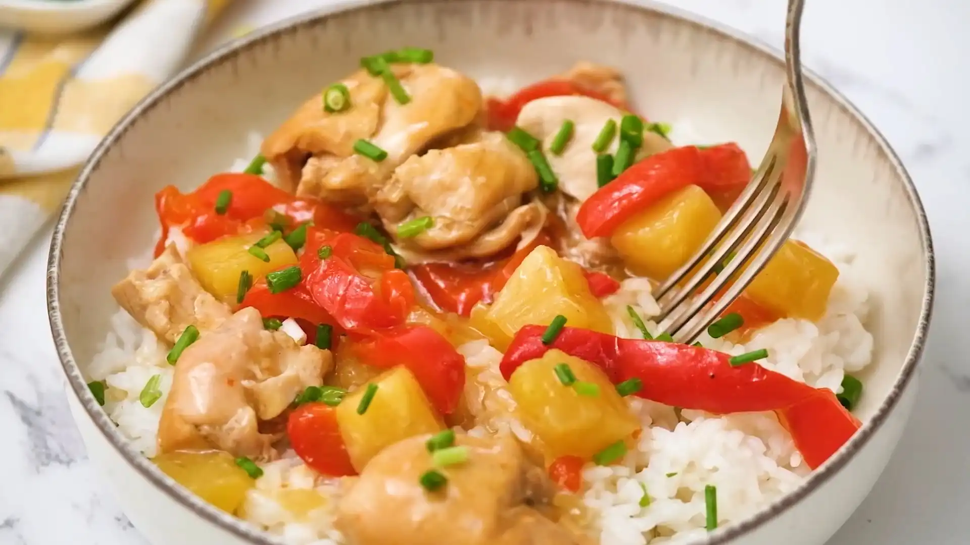 A bowl of Sweet Hawaiian Crockpot Chicken served over white rice, garnished with chopped green onions, featuring tender chicken, red bell peppers, and pineapple chunks in a savory-sweet sauce.