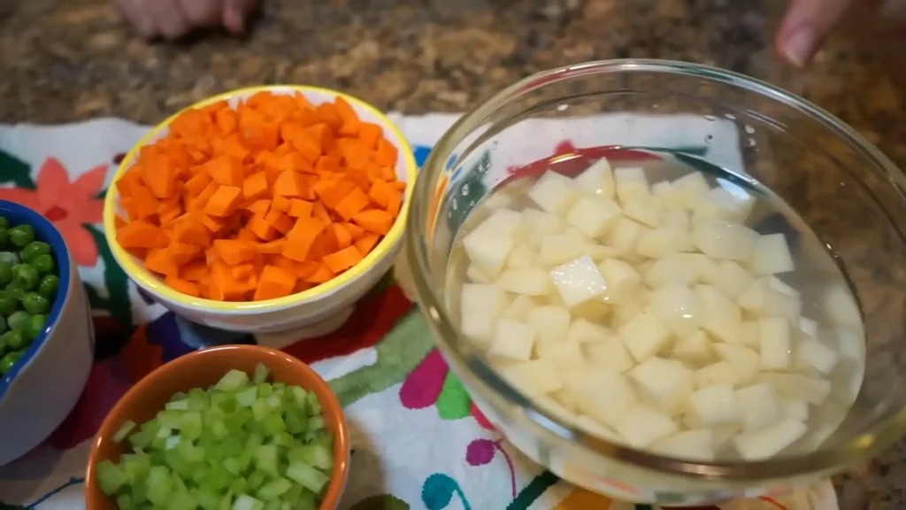 Diced vegetables including carrots, potatoes, peas, and celery, prepped for ensalada de pollo.