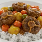 A plate of rabo encendido, a Cuban-style oxtail stew, served over white rice with potatoes, carrots, and green olives.