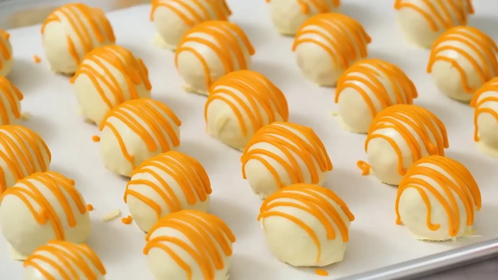 No-Bake Pumpkin Cheesecake Balls with orange drizzle on parchment paper