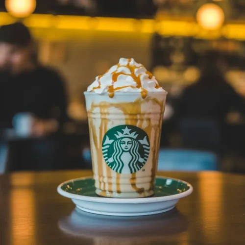 Butterbeer-style Starbucks Secret Menu drink with whipped cream and caramel drizzle in a clear cup on a saucer.