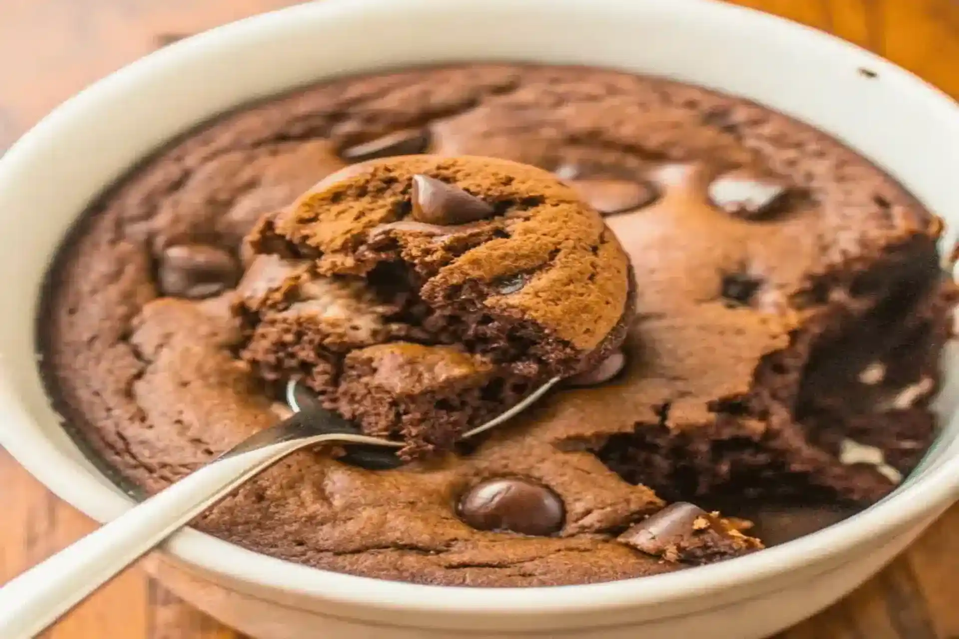 Delicious chocolate protein mug cake recipe served warm in a white mug with chocolate chips.